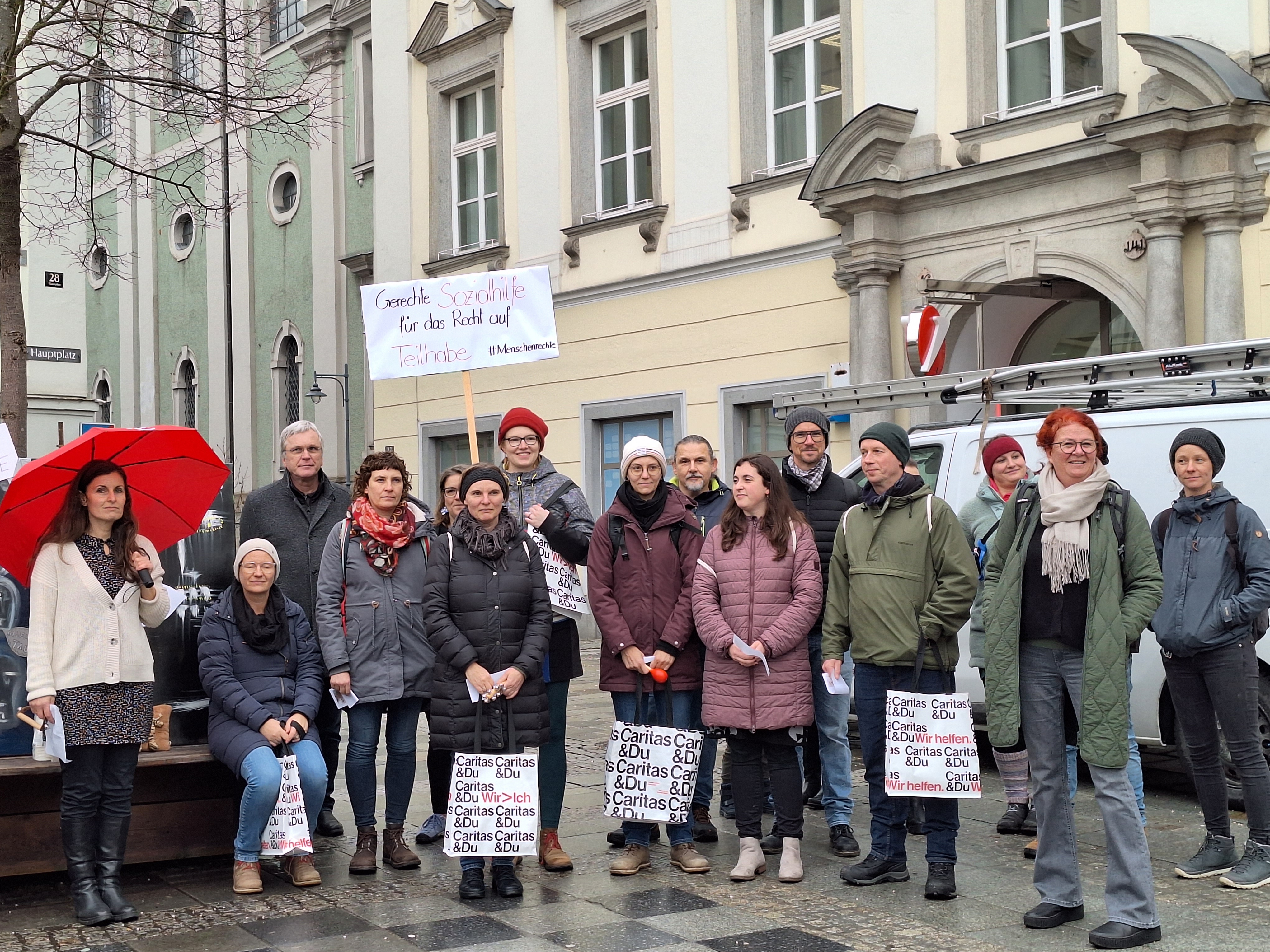 Eine Gruppe an Menschen protestiert am Linzer Hauptplatz gegen die oberösterreichische Sozialhilfe. Sie halten Schilder hoch. 
