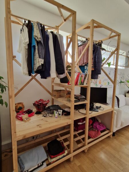 Eine offene Garderobe aus Holz. Darin hängen verschiedene Kleidungsstücke